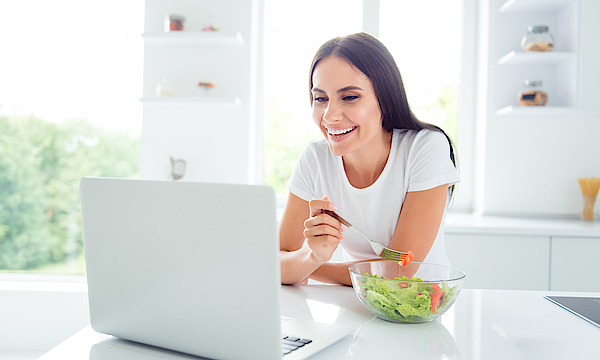 Eine junge Frau sitzt vor einem Laptop. Sie schaut auf den Bildschirm und lacht.