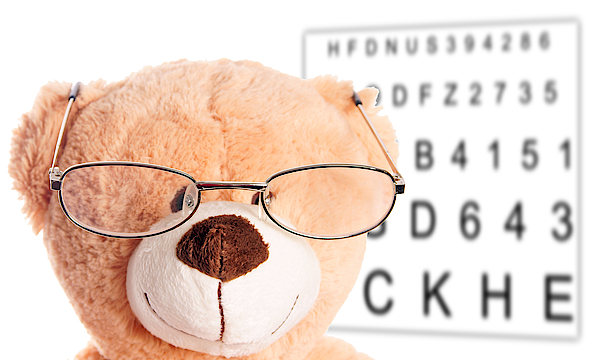Ein Taddybar hat eine Brille auf. Hinter ihm an der Wand sind die verschieden großen Buchstaben eines Sehtests.
