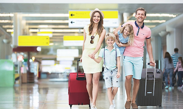 Eine Familie ist am Flughafen. Sie haben Koffer dabei. Sie sind auf dem Weg zum Abfluggate.